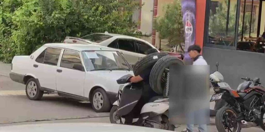 Otomobil lastiğini boynuna asan kuryenin ilginç taşıma yöntemi kameraya yansıdı