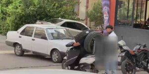 Otomobil lastiğini boynuna asan kuryenin ilginç taşıma yöntemi kameraya yansıdı