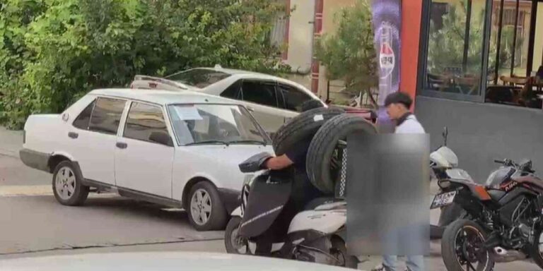 Otomobil lastiğini boynuna asan kuryenin ilginç taşıma yöntemi kameraya yansıdı
